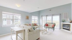 A spacious living room with a large window, a sofa, a coffee table, and a fireplace. - Charming condo with nearby golf, outdoor pool & close to the beach (Ocean View)