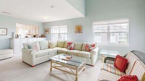 A living room with a sectional sofa, a glass coffee table, and a striped sofa. - Charming condo with nearby golf, outdoor pool & close to the beach (Ocean View)