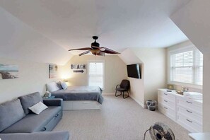 Ein Schlafzimmer mit Bett, Deckenventilator, Fernseher, Kommode und Fenster.
