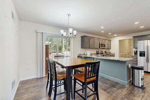 A modern kitchen with a dining area, featuring a central island, built-in appliances, and a chandelier. - Holy Park house w/deck, patio, grill, close to beach & restaurants. (Ocean View)