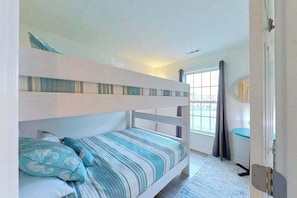A bunk bed room with a window, a door, and a small table. - Townhomes of Providence spacious townhouse w/shared pool, deck, W/D (Ocean View)