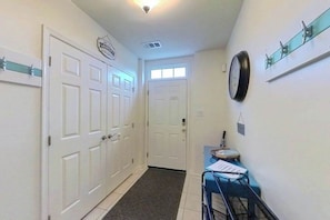 A hallway with white doors, a small table with papers, a clock, and a window. - Townhomes of Providence spacious townhouse w/shared pool, deck, W/D (Ocean View)