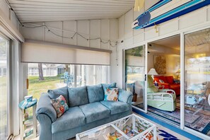 A room with a grey sofa, a glass coffee table, and a sliding glass door leading to an outdoor area. - Mallard Lakes condo w/community pool, hot tub, tennis & basketball court (Selbyville)
