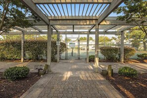 A covered outdoor area with a paved walkway, metal fencing, and greenery.
