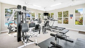Une salle de sport équipée de divers appareils d’exercice, dotée de grandes fenêtres et d’un ventilateur de plafond.