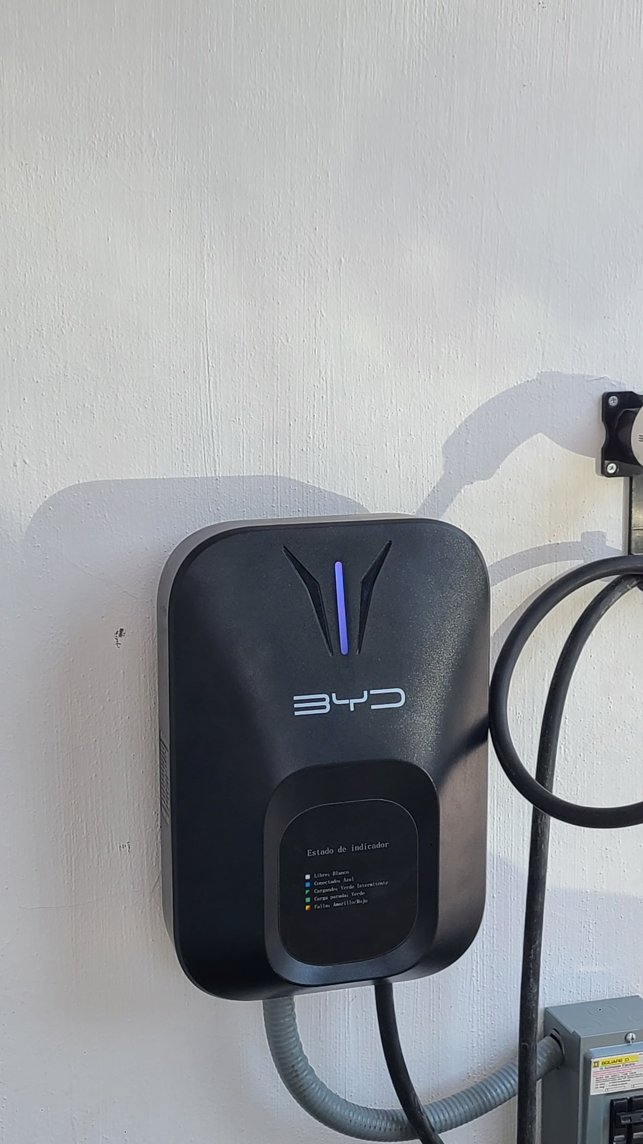 A wall-mounted charging station with a digital indicator panel, connected by a cable.