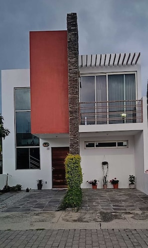 A modern two-story building with a balcony, large windows, and potted plants.