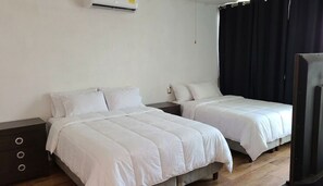 A hotel room with two beds, a dark wooden nightstand, a white wall, and a black curtain.
