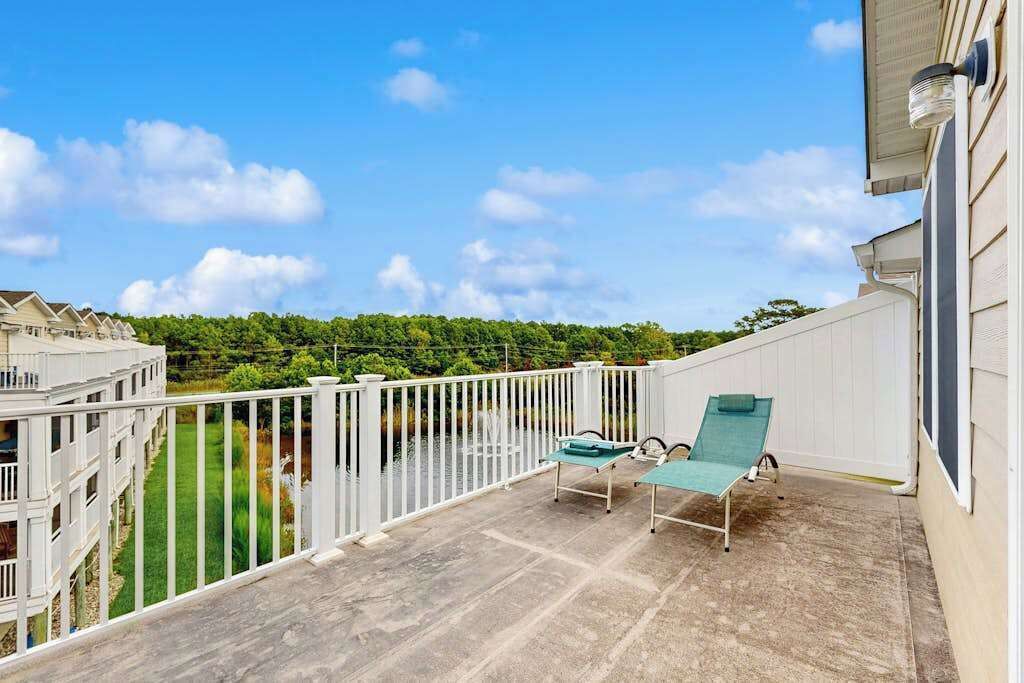 Un balcon doté d’une balustrade blanche, de deux fauteuils de jardin verts et offrant une vue sur une pelouse verdoyante et des arbres.