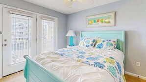 Ein Schlafzimmer mit Bett, Deckenventilator, Fenster mit Jalousien und einem Wandbild.