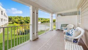Eine überdachte Veranda mit weißen Geländern, Blick ins Grüne und zwei Korbstühle mit Kissen.
