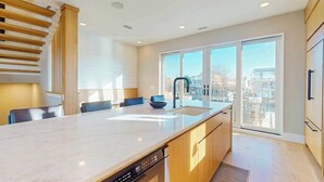 Una cocina moderna con una isla grande, electrodomésticos integrados y un ventanal corredero que da a un balcón.