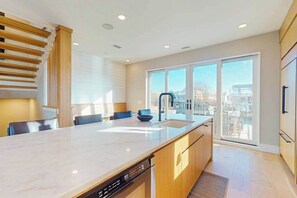 Eine moderne Küche mit einer großen Kochinsel, integrierten Geräten und einer Glastür zum Balkon.