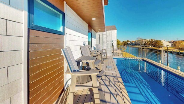 Zona junto a la piscina con sillones reclinables, una terraza de madera y vista a un cuerpo de agua.