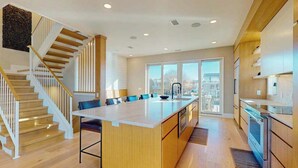 Una cocina moderna con una isla central, suelo de madera, una escalera y ventanas grandes.