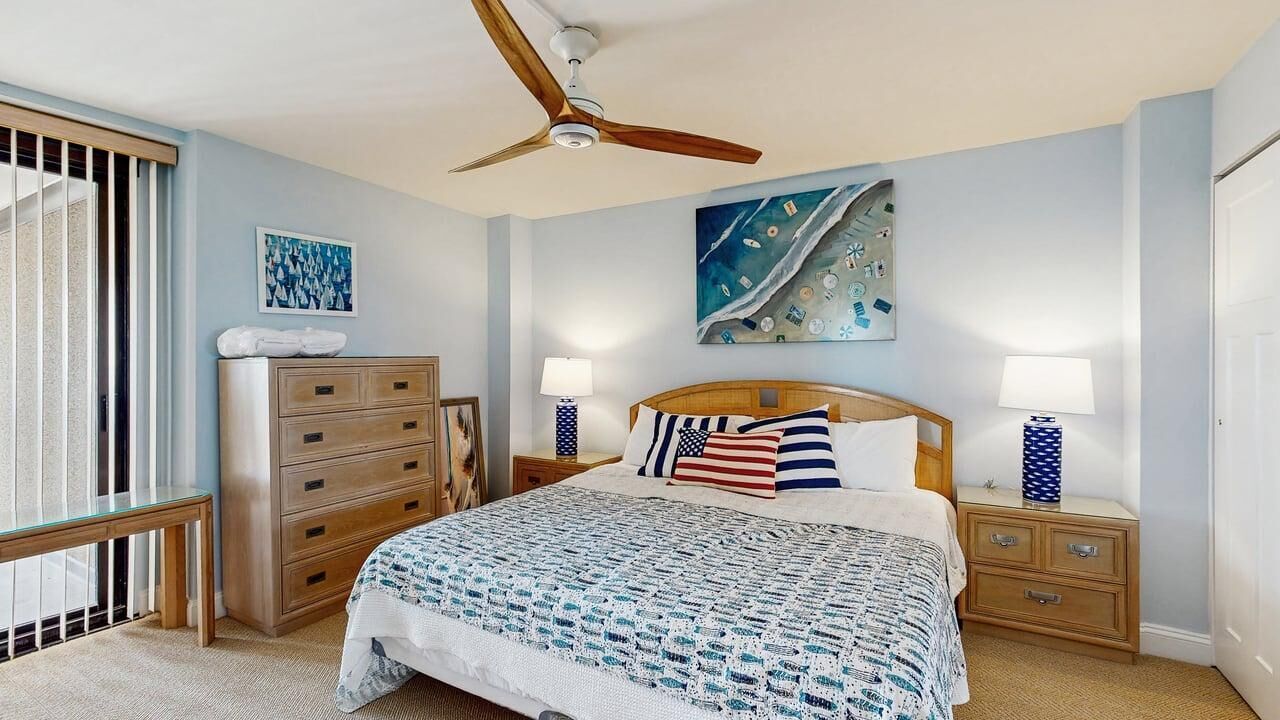 Un dormitorio con una cama, un aparador de madera, un ventilador de techo y dos mesitas de noche con lámparas.