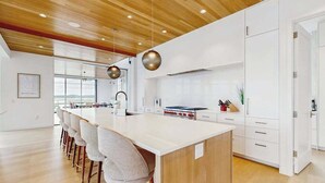A modern kitchen with a central island, bar stools, and a wooden ceiling. - Bayview Park bay front house w/private pool, amazing bay views, deck, balcony (Bethany Beach)