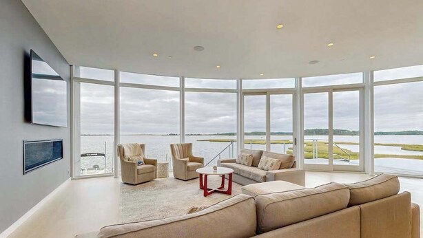 A spacious living room with a large window, a sofa set, and a coffee table. - Bayview Park bay front house w/private pool, amazing bay views, deck, balcony (Bethany Beach)