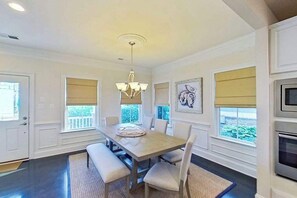 A dining area with a wooden table, chairs, a chandelier, and large windows with blinds. - Bayside Resort townhouse w/community pools, hot tubs, tennis & on-site golf (Selbyville)