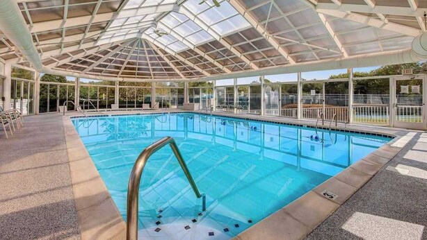 Une piscine intérieure dotée d’un toit en verre, d’un espace dégagé autour du bassin et d’un panneau de signalisation indiquant clairement la sortie.