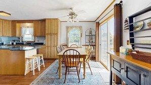Cozinha com armários de madeira, uma mesa de jantar com cadeiras, um ventilador de teto e uma janela com cortinas.