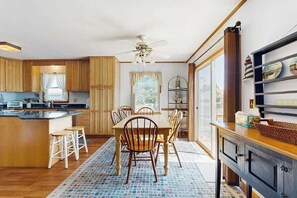 A kitchen with wooden cabinets, a dining table with chairs, a ceiling fan, and a window with curtains. - South Bethany Canal Front home, dock, deck, grill (Bethany Beach)