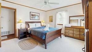 Quarto com cama, luminárias de cabeceira, ventoinha no teto, cômoda e espelho.