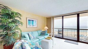 A hotel room with a large window, a sofa, a chair, a potted plant, and a painting. - Sea Colony oceanfront 7th-floor condo with pool & tennis/basketball courts (Bethany Beach)