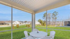 A covered patio with a table and chairs, large windows, and a view of houses and a road. - Milo's Haven townhouse w/community pool, grill, close to restaurants (Frankford)