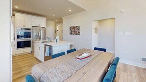 A modern kitchen with white cabinets, a stainless steel refrigerator, and a dining area with a wooden table and blue chairs. - Milo's Haven townhouse w/community pool, grill, close to restaurants (Frankford)