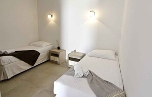 Ein Doppelzimmer mit zwei Betten, einem Nachttisch, einer Lampe und einer Gitarre.