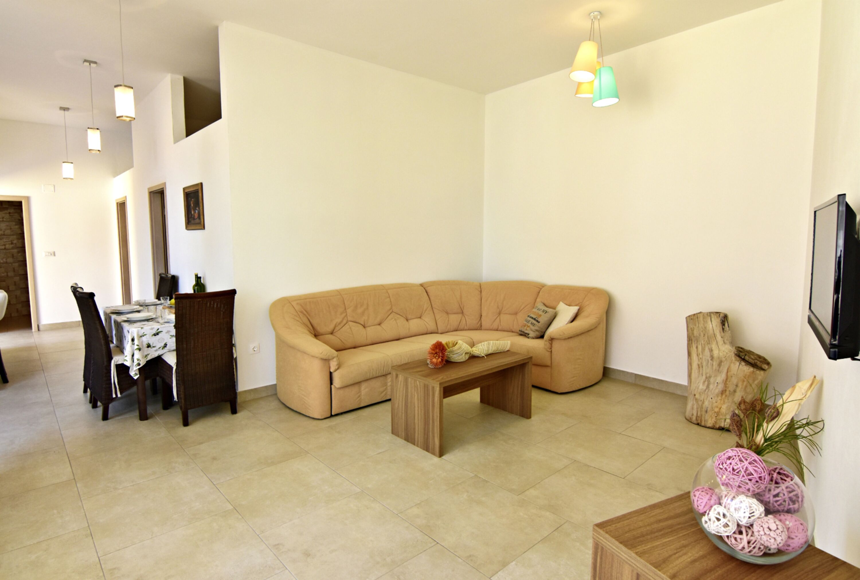 A living room with a sofa, a coffee table, a dining table with chairs, and a television.
