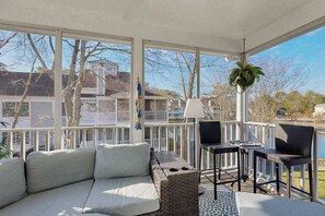 A covered outdoor seating area with a sofa, two tables, and chairs, overlooking a body of water and residential buildings. - Sea Colony Tennis 2nd-floor condo w/community pools, tennis/pickleball, gym (Bethany Beach)
