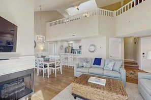 A spacious living area with a high ceiling, a dining table, a sofa, and a fireplace. - Sea Colony Tennis 2nd-floor condo w/community pools, tennis/pickleball, gym (Bethany Beach)