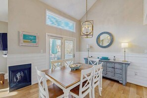 A dining area with a wooden table, white chairs, a fireplace, and a view of the outdoors. - Sea Colony Tennis 2nd-floor condo w/community pools, tennis/pickleball, gym (Bethany Beach)