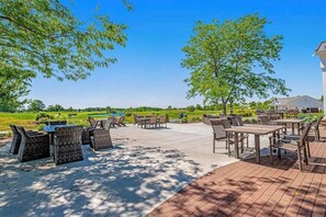 Eine Außenpatio-Terrasse mit Tischen und Stühlen, umgeben von Bäumen und Blick auf einen Golfplatz.