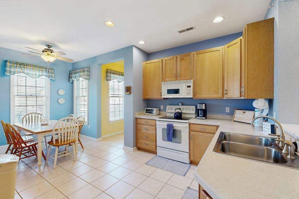 A kitchen with wooden cabinets, a microwave, a stove, a sink, and a dining area with chairs and a table.
