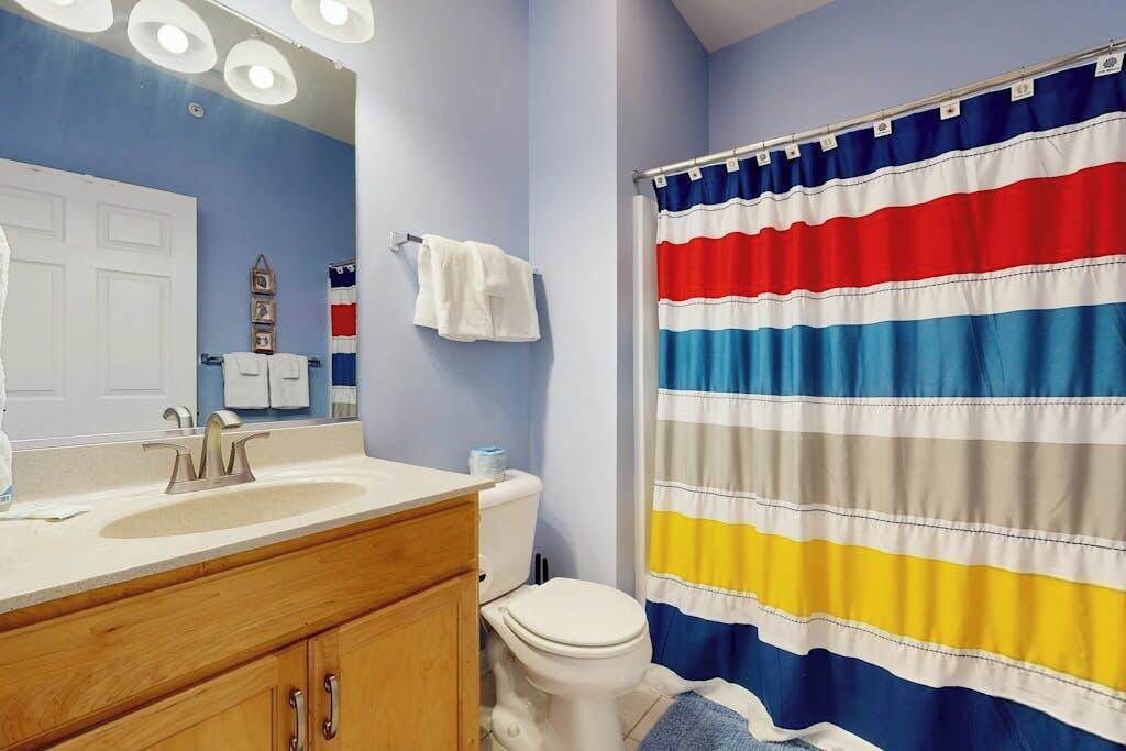 Un bagno con tenda da doccia a righe, un lavandino, un water e uno specchio.