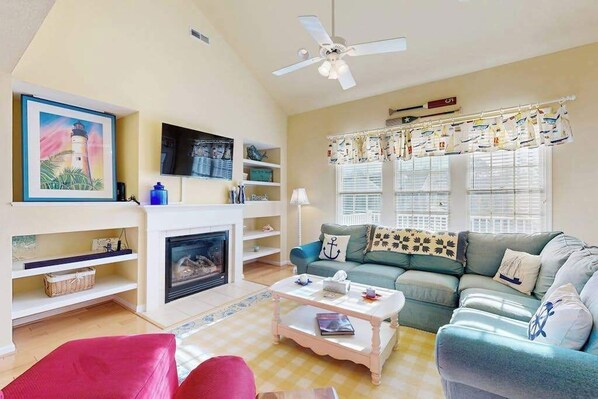 Ein Wohnzimmer mit Kamin, Deckenventilator, Sofa, Couchtisch und Wandfernseher.