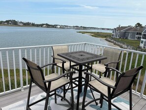 A deck with a table and chairs overlooking a body of water. - Newly Remodeled 2026 Waterfront Condo | Indian Inlet Bridge Views | Sleeps 10 (Ocean View)