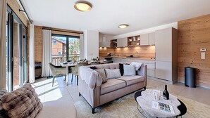A modern living room with a sofa, a dining area with chairs, a kitchen with wooden cabinets, and a large window. - Rennes - Apartment - Sleeps 6 - Jacuzzi (Les Gets)