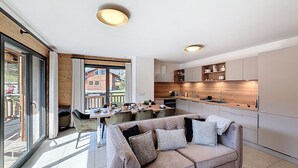 A modern kitchen with wooden cabinets, a dining area with a table and chairs, and a sofa with cushions. - Rennes - Apartment - Sleeps 6 - Jacuzzi (Les Gets)
