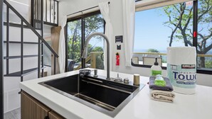 A modern kitchen with a stainless steel sink, a window with a view, and a Kirkland Premium Towels bottle. - The Pine- Smoky Mountains View Tiny House w/ Hot Tub & Deck (Tallassee)