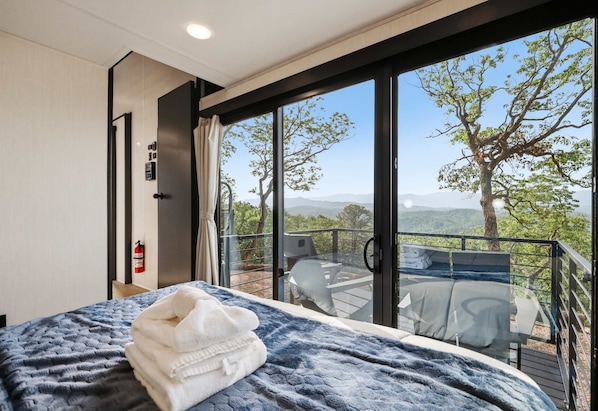 A bedroom with a large bed, a fire extinguisher, and a balcony with a table and chairs.