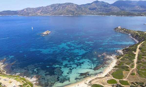 Luftaufnahme einer Küstenlandschaft mit klarem, blauem Wasser, felsigem Gelände und einem Pfad zum Strand.