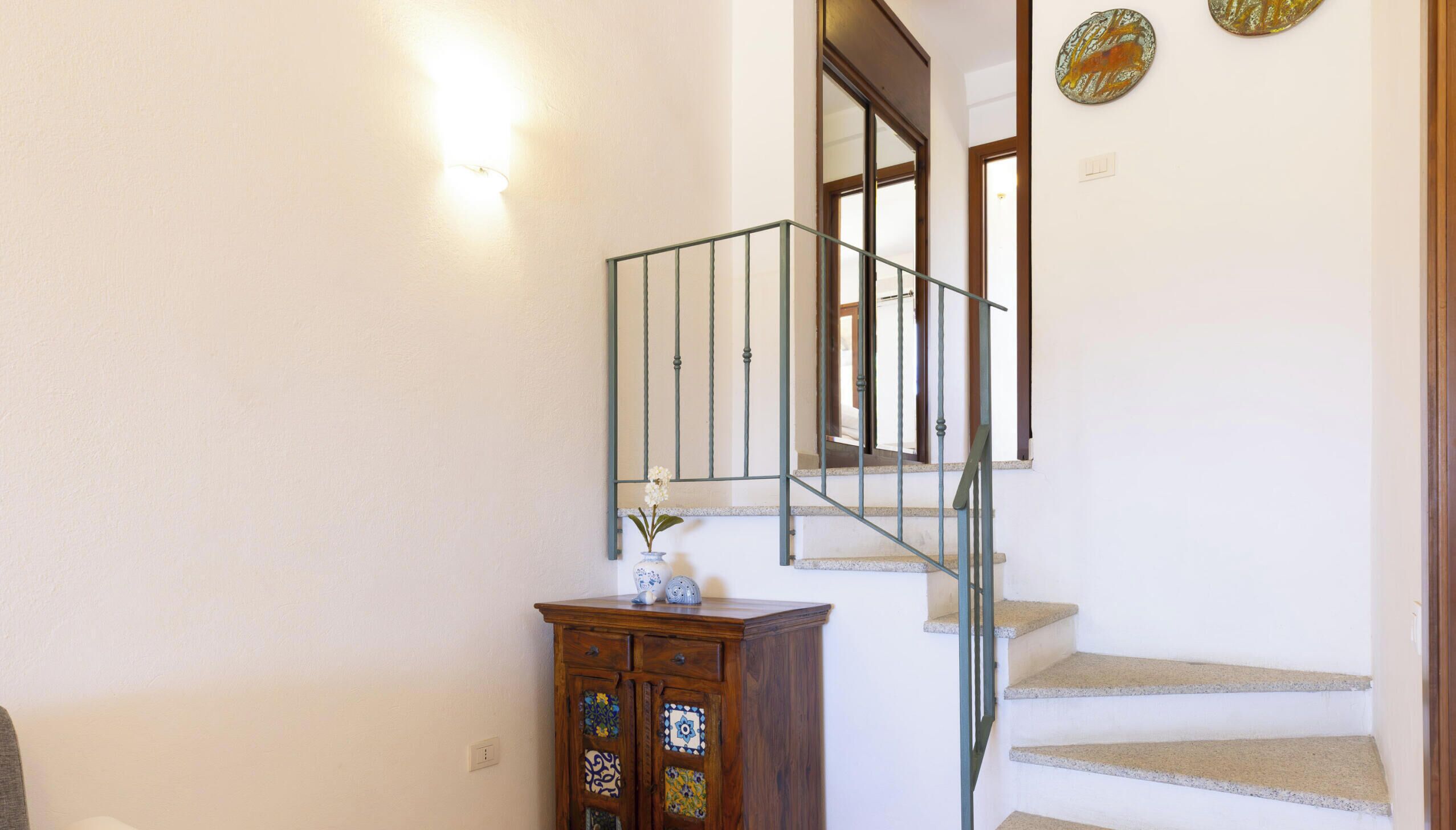 Eine Treppe mit Metallgeländer, ein Holzschrank mit dekorativen Fliesen und eine Wandleuchte.