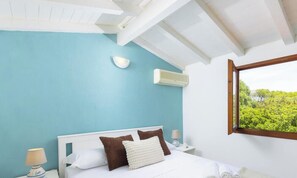 Ein Schlafzimmer mit einem Bett, einem weißen Kopfteil, blauen Wänden, einem Fenster mit Blick und einer Wand-Klimaanlage.