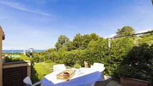 En terrasse med et spisebord, omgivet af frodig vegetation og udsigt til havet.