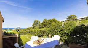Eine Terrasse mit Esstisch, umgeben von üppiger Vegetation und Blick aufs Meer.