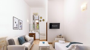 En moderne stue med sofa, sofabord og fjernsyn. En trappe fører op til en balkon.